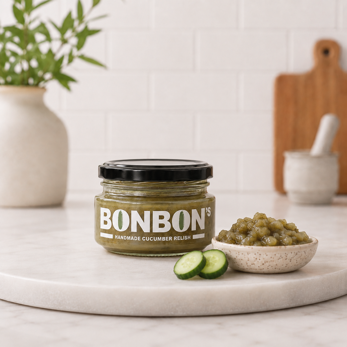 Jar of BonBon's handmade cucumber relish beside a filled bowl and fresh cucumber slices