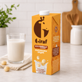 Orange carton of Giraf vanilla macadamia drink beside a filled glass and macadamia nuts
