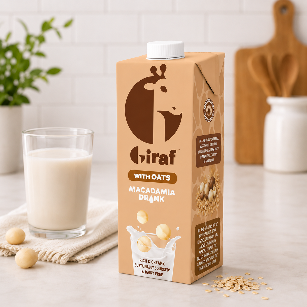 Giraf oat macadamia drink carton beside a glass of creamy plant milk on a kitchen counter