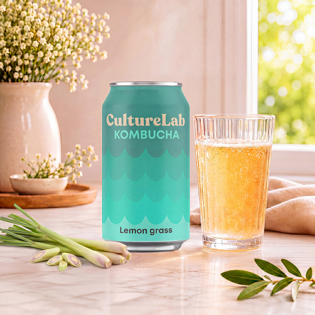 Turquoise can of lemongrass kombucha beside a glass of amber kombucha and fresh lemongrass