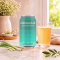 Turquoise can of lemongrass kombucha beside a glass of amber kombucha and fresh lemongrass