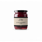 Glass jar of red strawberry jam with a black lid and cream label, front view